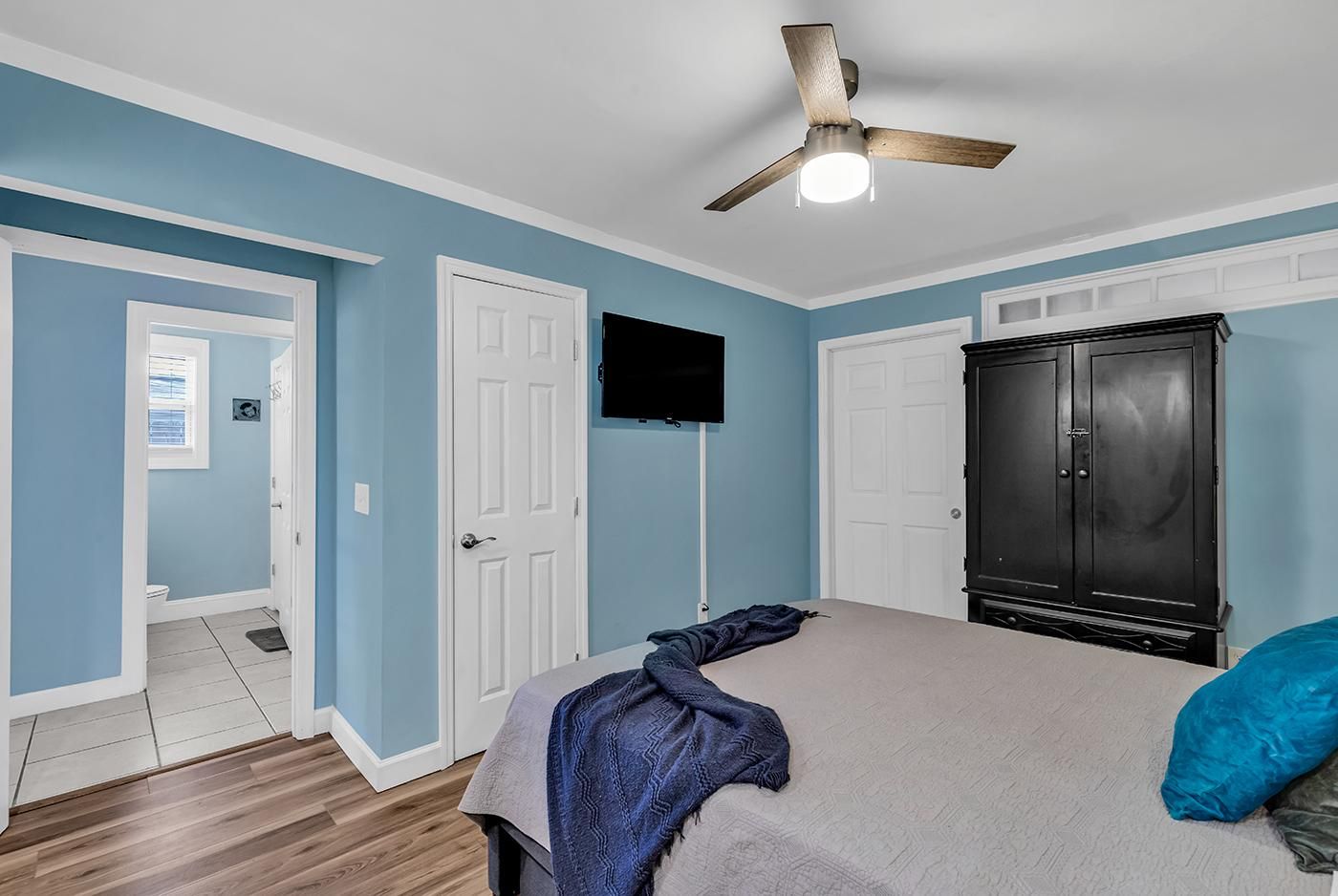 A bedroom with a bed, a wardrobe, a television, and a ceiling fan.
