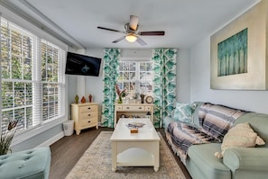 A living room with a television, a ceiling fan, a sofa, a coffee table, and a window with blinds.