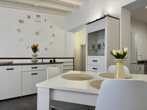 A modern kitchen with white cabinetry, a wall clock, and a dining table with placemats. - New Listing (Cinisi)