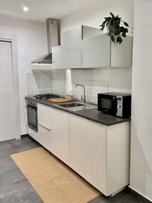 A modern kitchen with white cabinets, a gas stove, a microwave, and a sink. - New Listing (Cinisi)