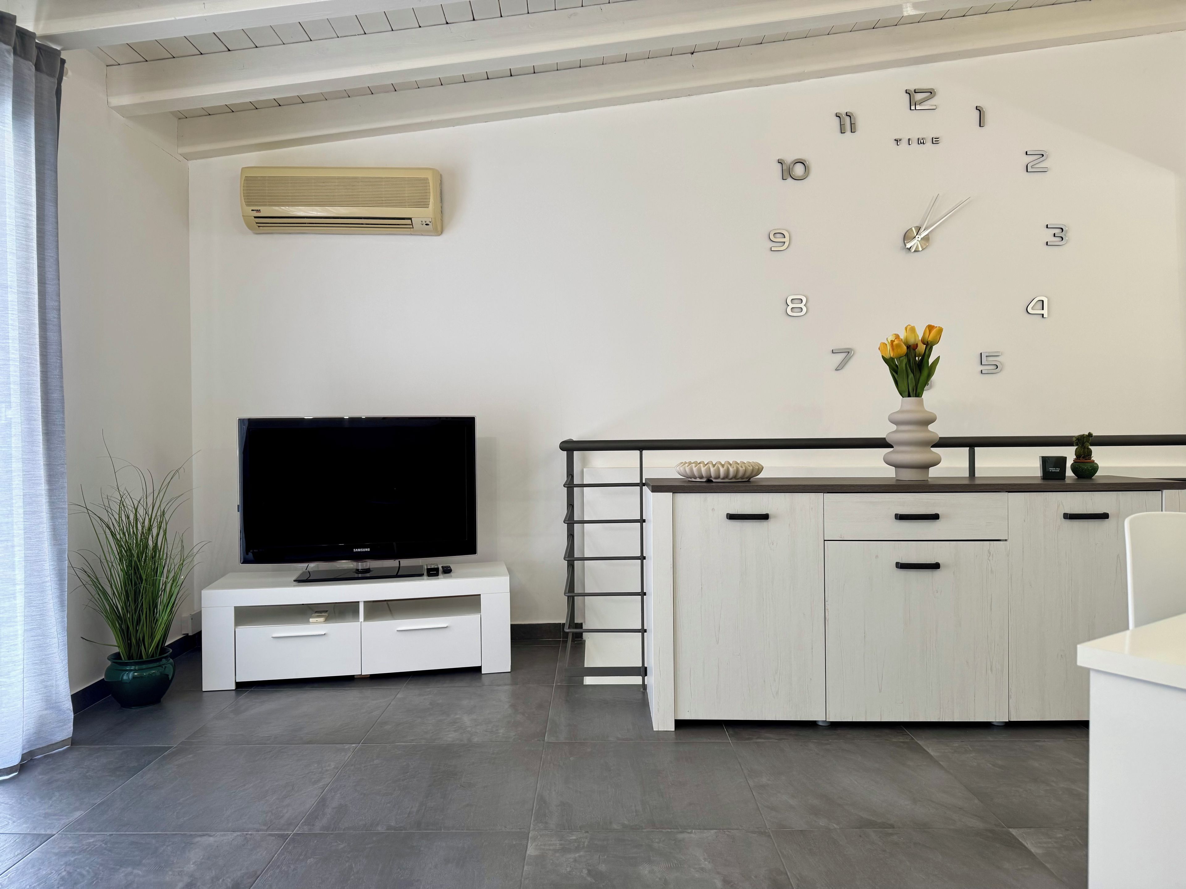 A modern living room with a flat-screen TV, a white cabinet, a clock, and a potted plant.