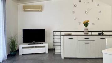 A modern living room with a flat-screen TV, a white cabinet, a clock, and a potted plant.