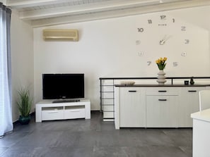 A modern living room with a flat-screen TV, a white cabinet, a clock, and a potted plant. - New Listing (Cinisi)