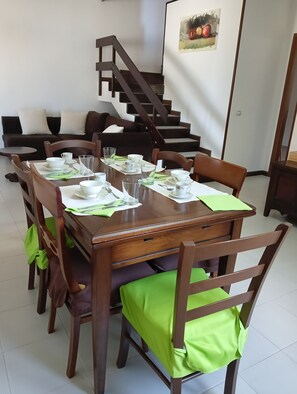 A dining area with a wooden table set for four, surrounded by chairs with green cushions. A staircase is visible in the background. - Bed and Breakfast 'Casa Misè -  Pepe E Zafferano' with Shared Terrace, Wi-Fi and Air Conditioning (Poggio dei Pini)