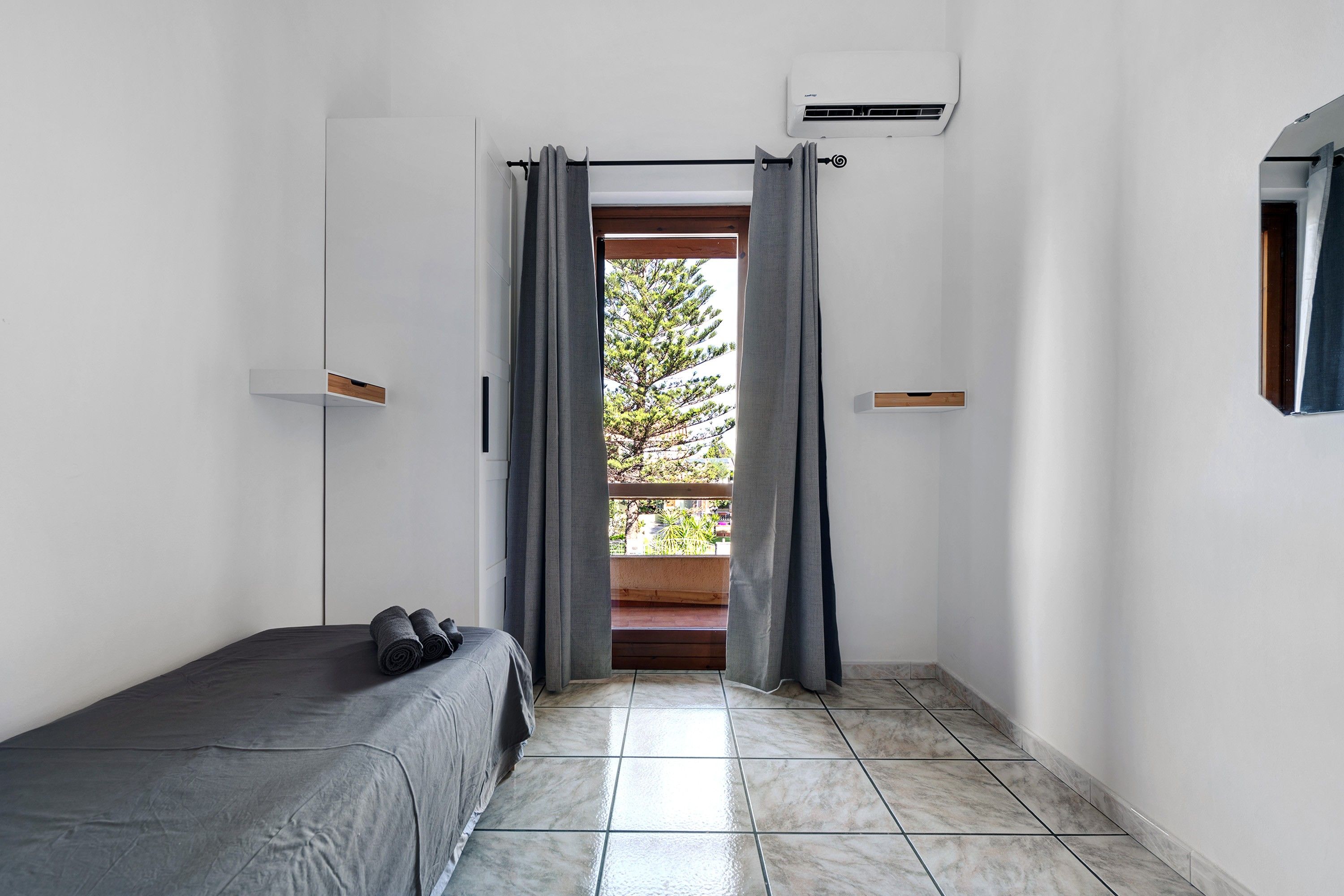 Una camera da letto con un letto, una finestra con tende, un tavolino e vista sugli alberi.