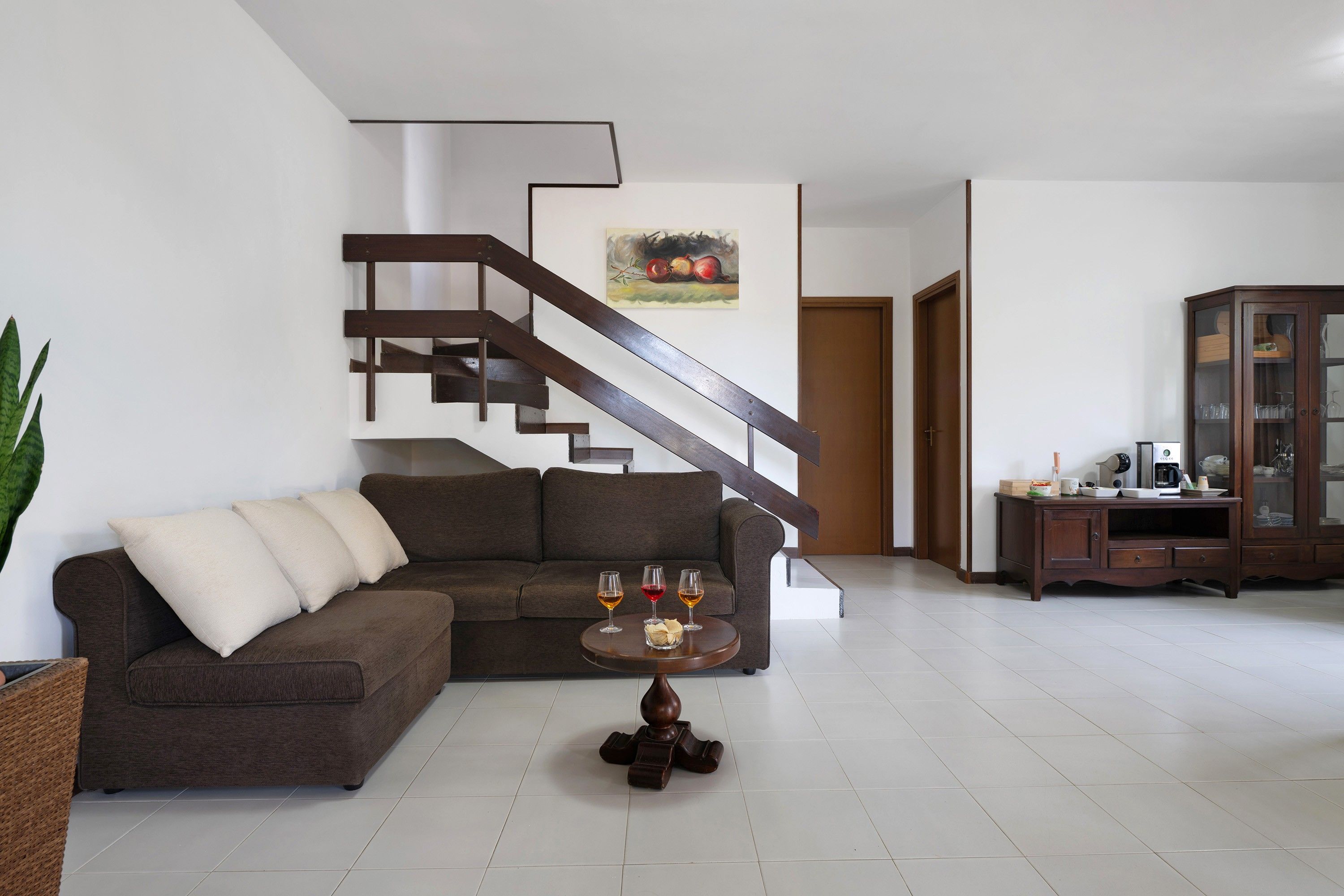 Una sala de estar moderna con un sofá seccional marrón, una mesa de centro con vasos, y una escalera con un cuadro en la pared.