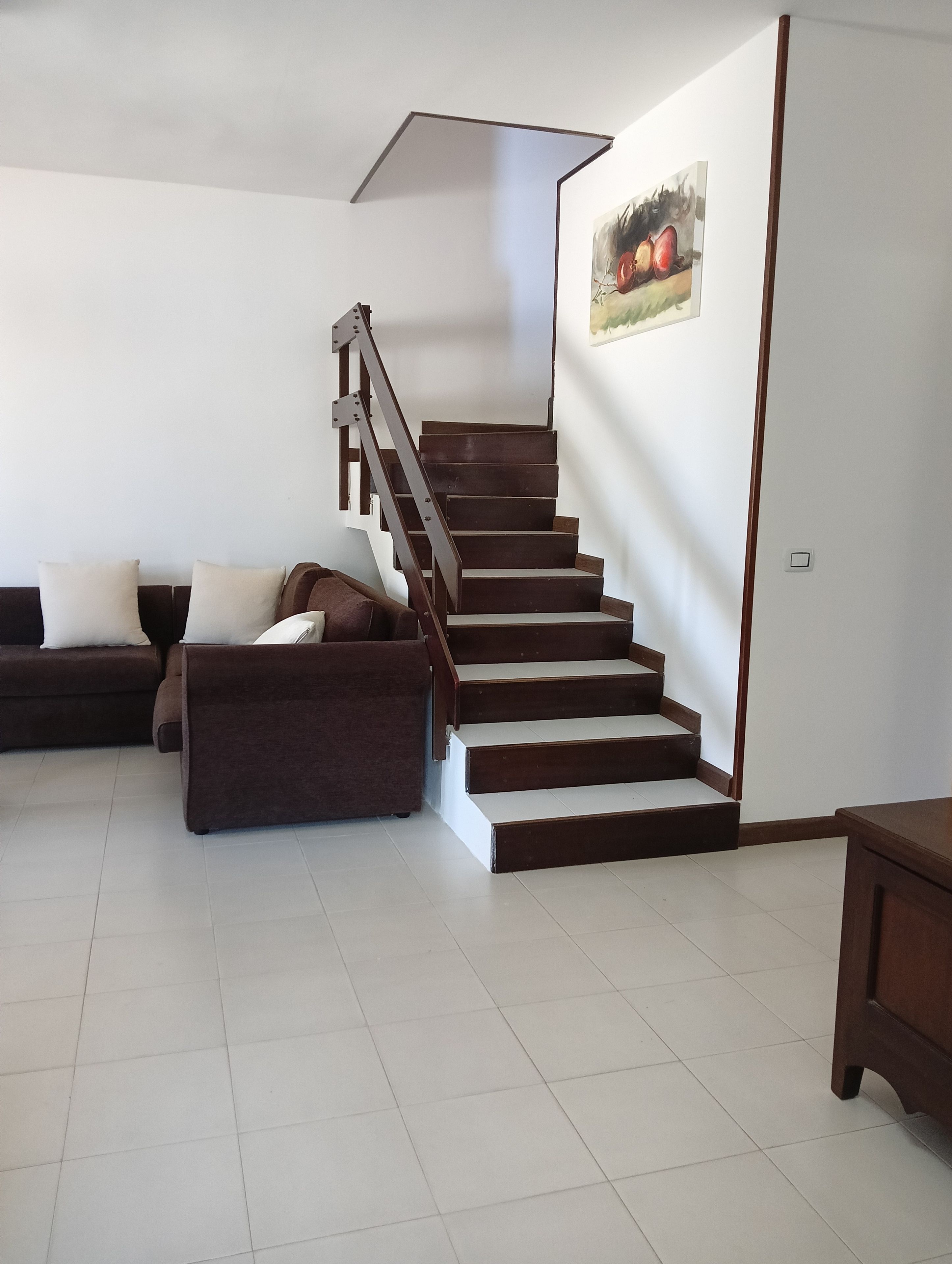Uma sala de estar com escada, sofá e um quadro na parede.