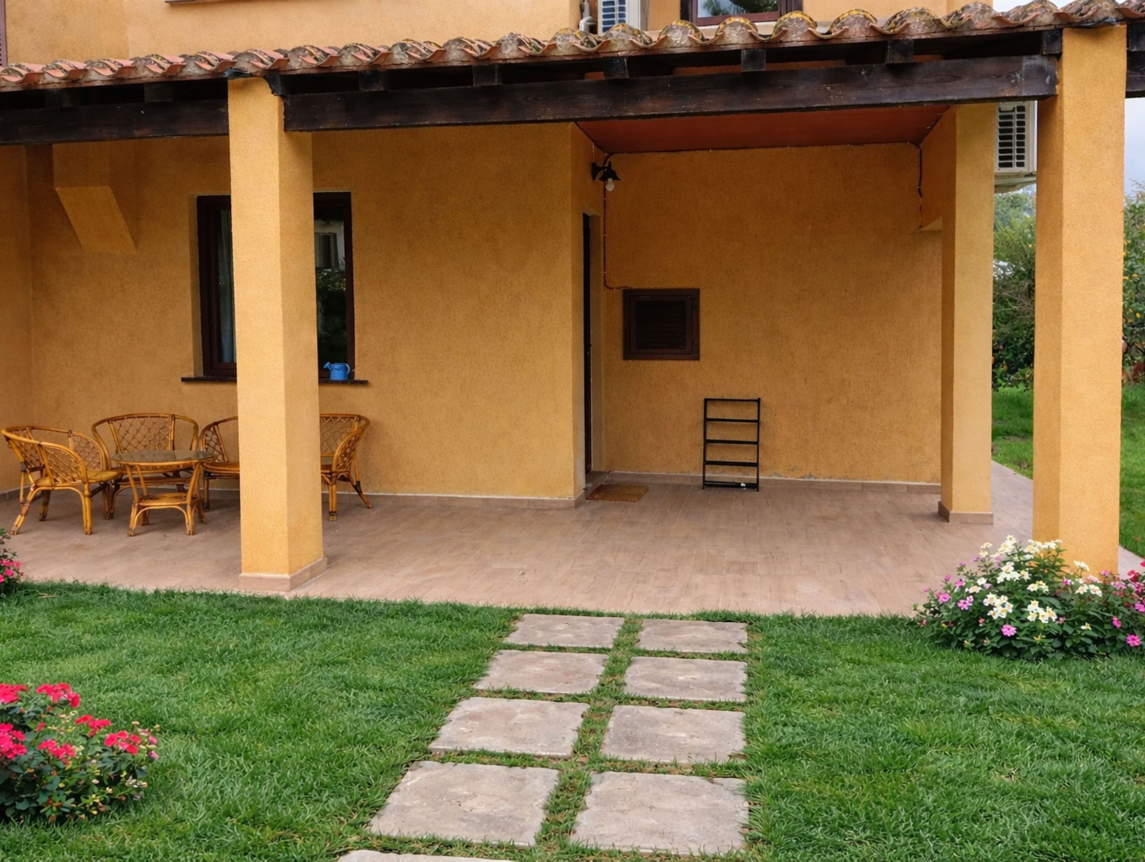 Uma área de varanda coberta, com assentos e um pequeno jardim.