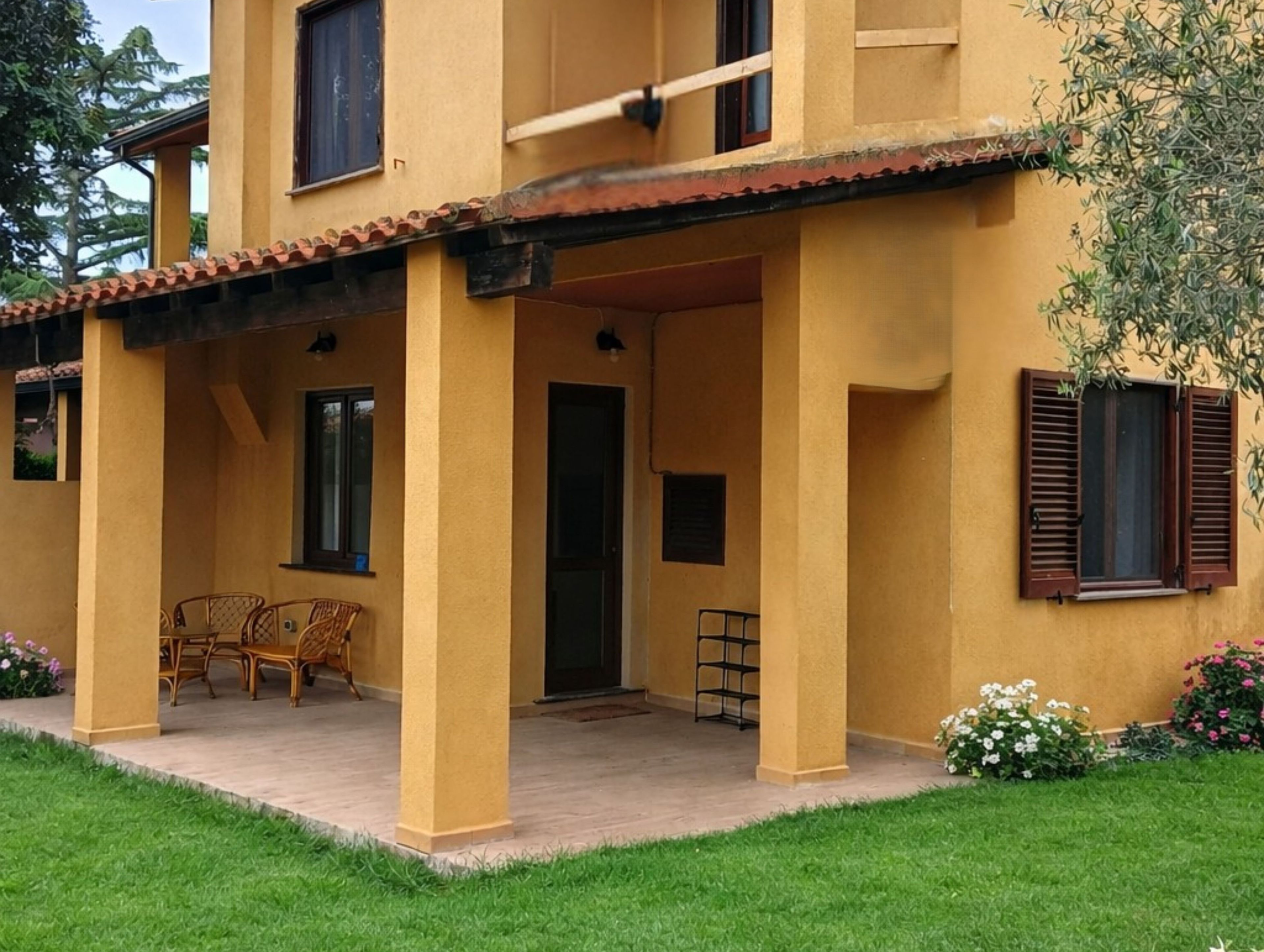 A two-story building with a covered patio area, a door, and a window with shutters.