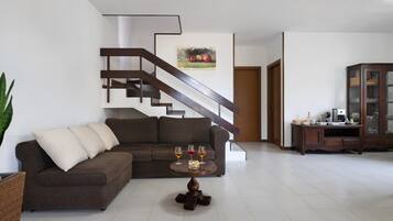 Una sala de estar moderna con un sofá seccional marrón, una mesa de centro con vasos, y una escalera con un cuadro en la pared.