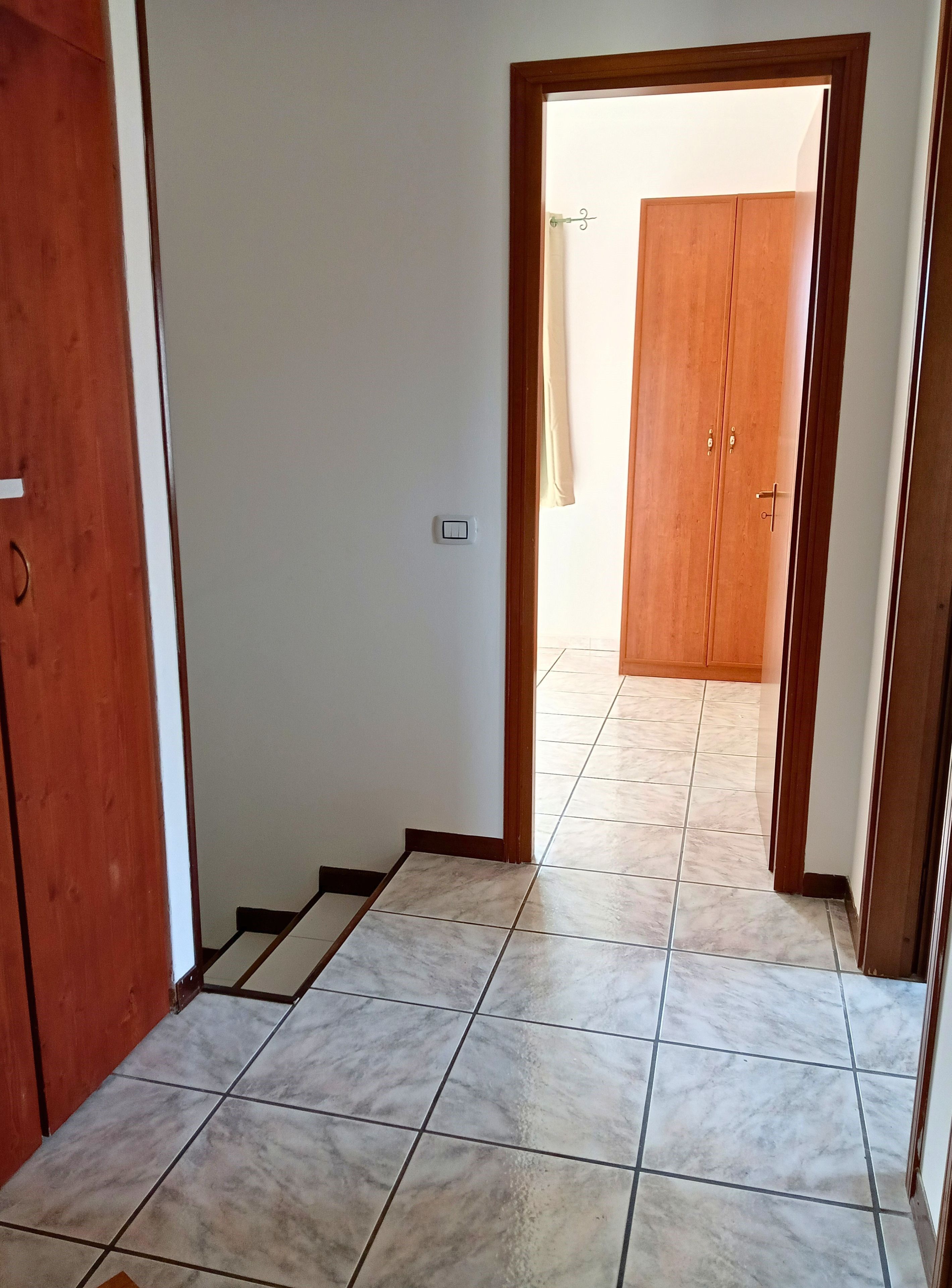 A hallway with a tiled floor, a wooden door on the left, and a wooden door at the end.