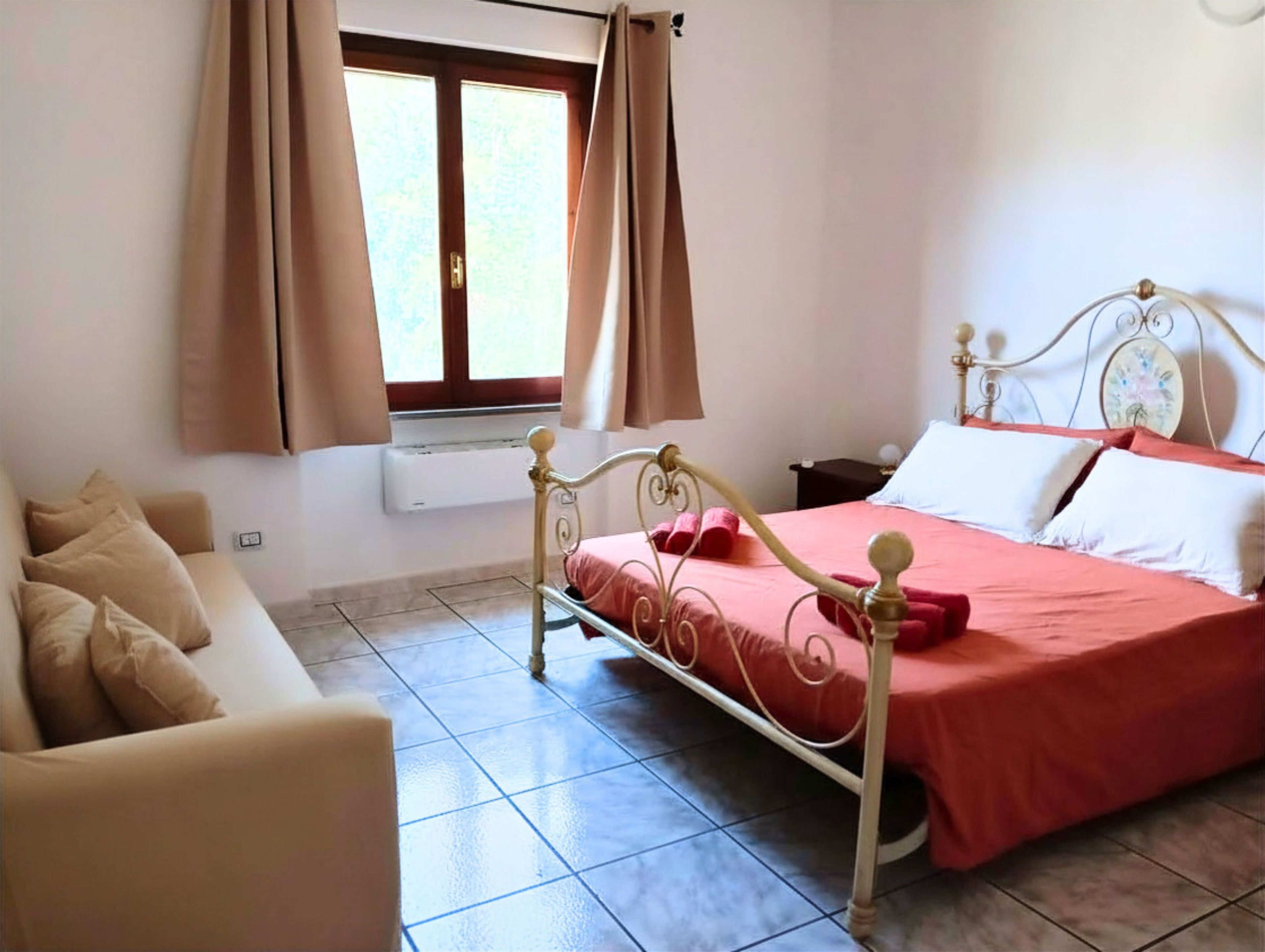 A bedroom with a bed, a chair, a window with curtains, and an air conditioning unit.