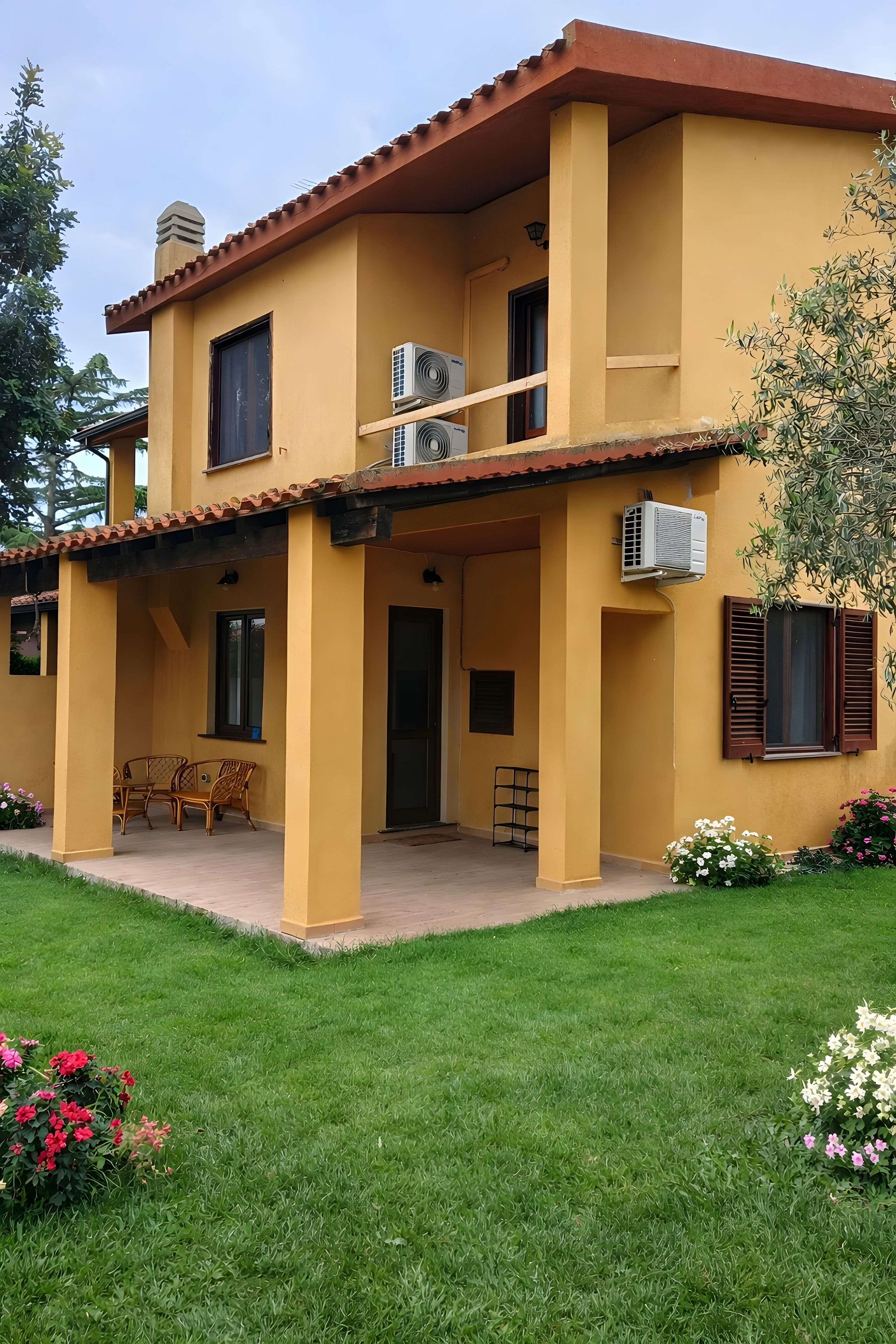 Ein zweistöckiges Haus mit flachem Dach, Klimaanlagen und einer kleinen Terrasse mit Möbeln.