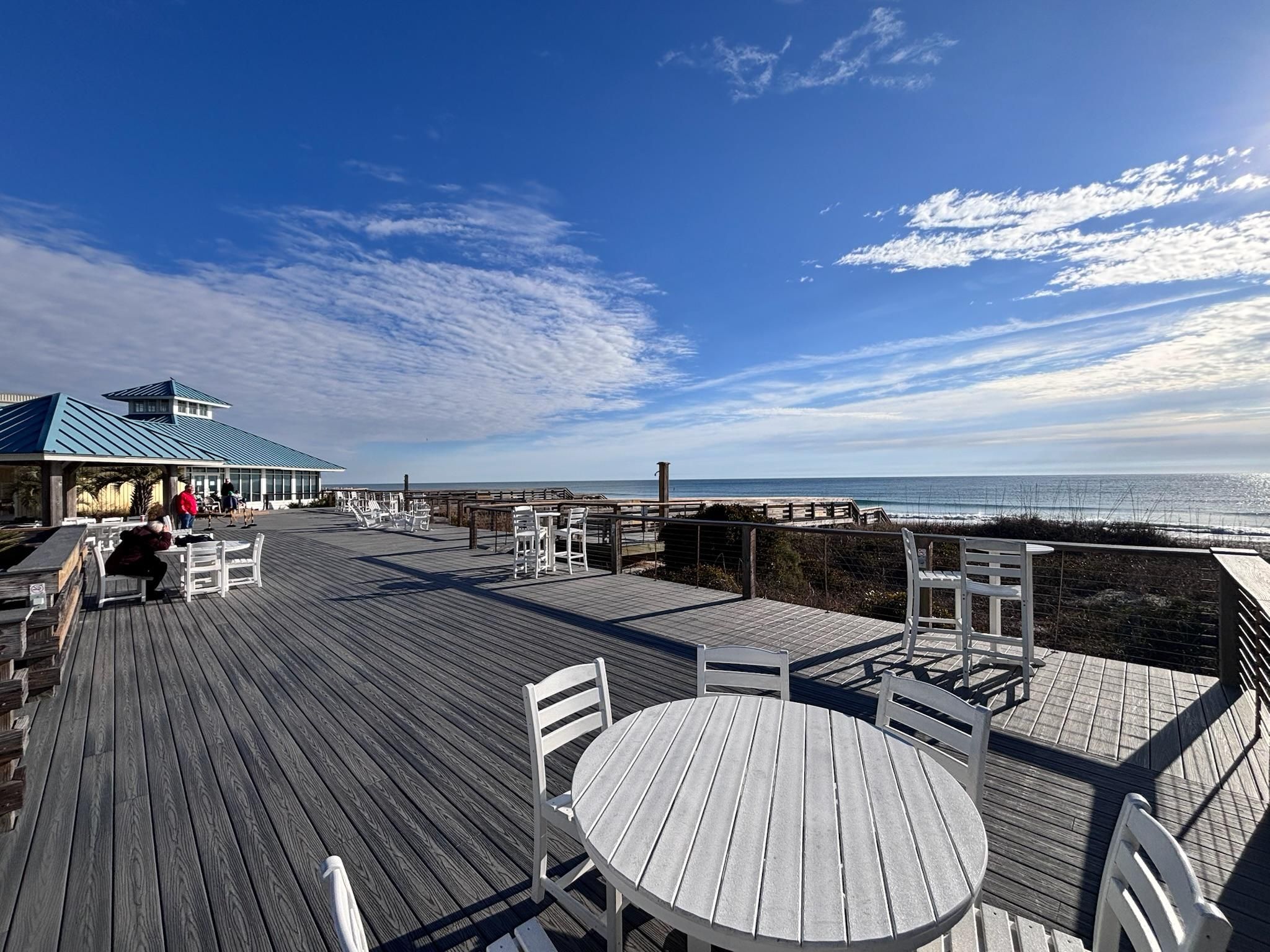 Une terrasse en bois, avec des tables et des chaises, donnant sur une plage.
