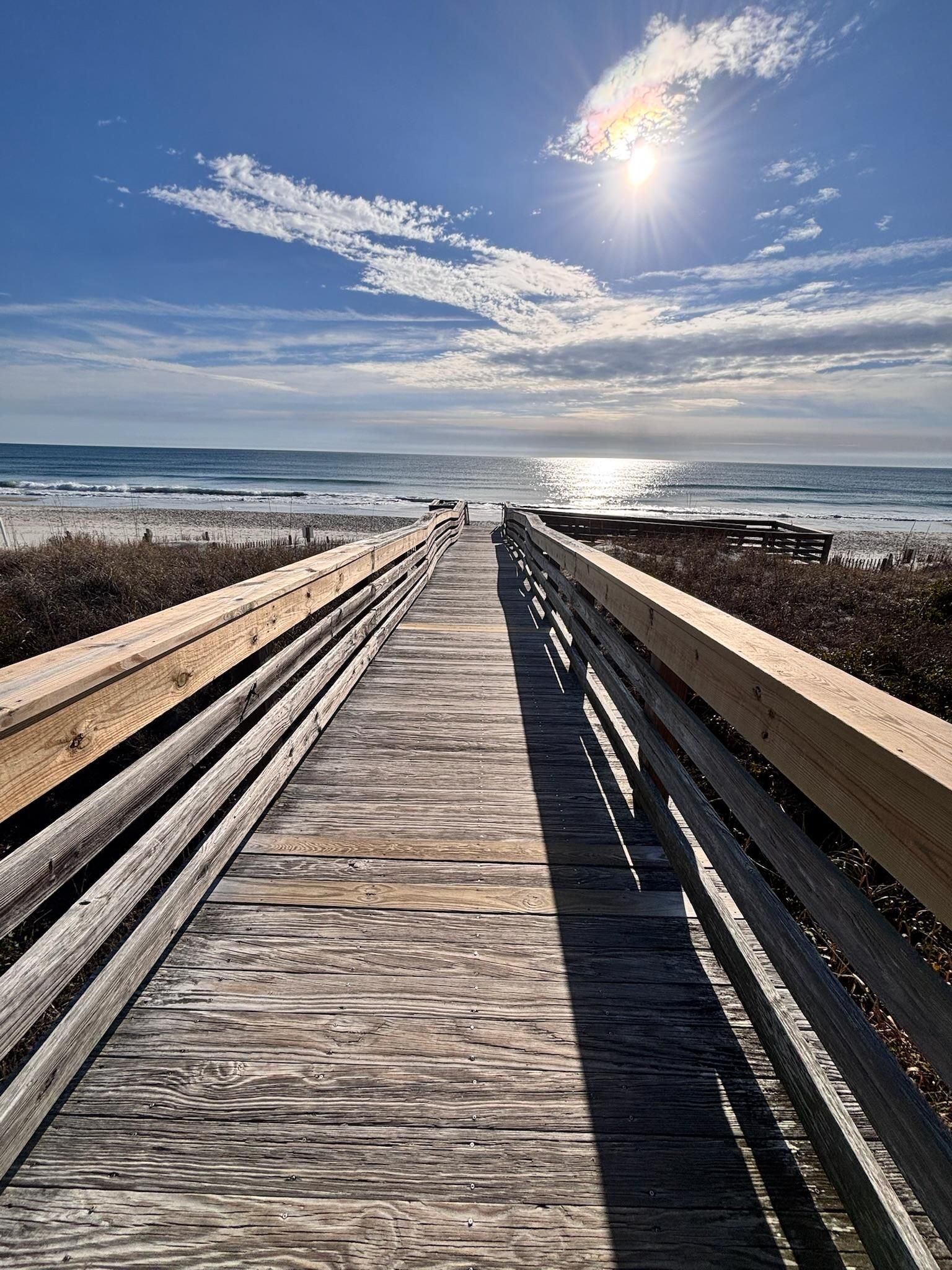 Un paseo marítimo de madera que conduce a una playa con cielo despejado y sol.