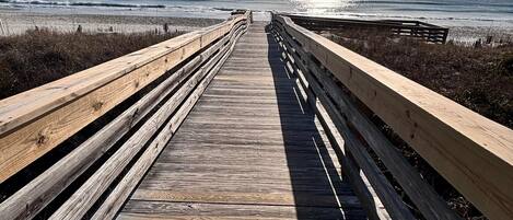 Un paseo marítimo de madera que conduce a una playa con cielo despejado y sol.