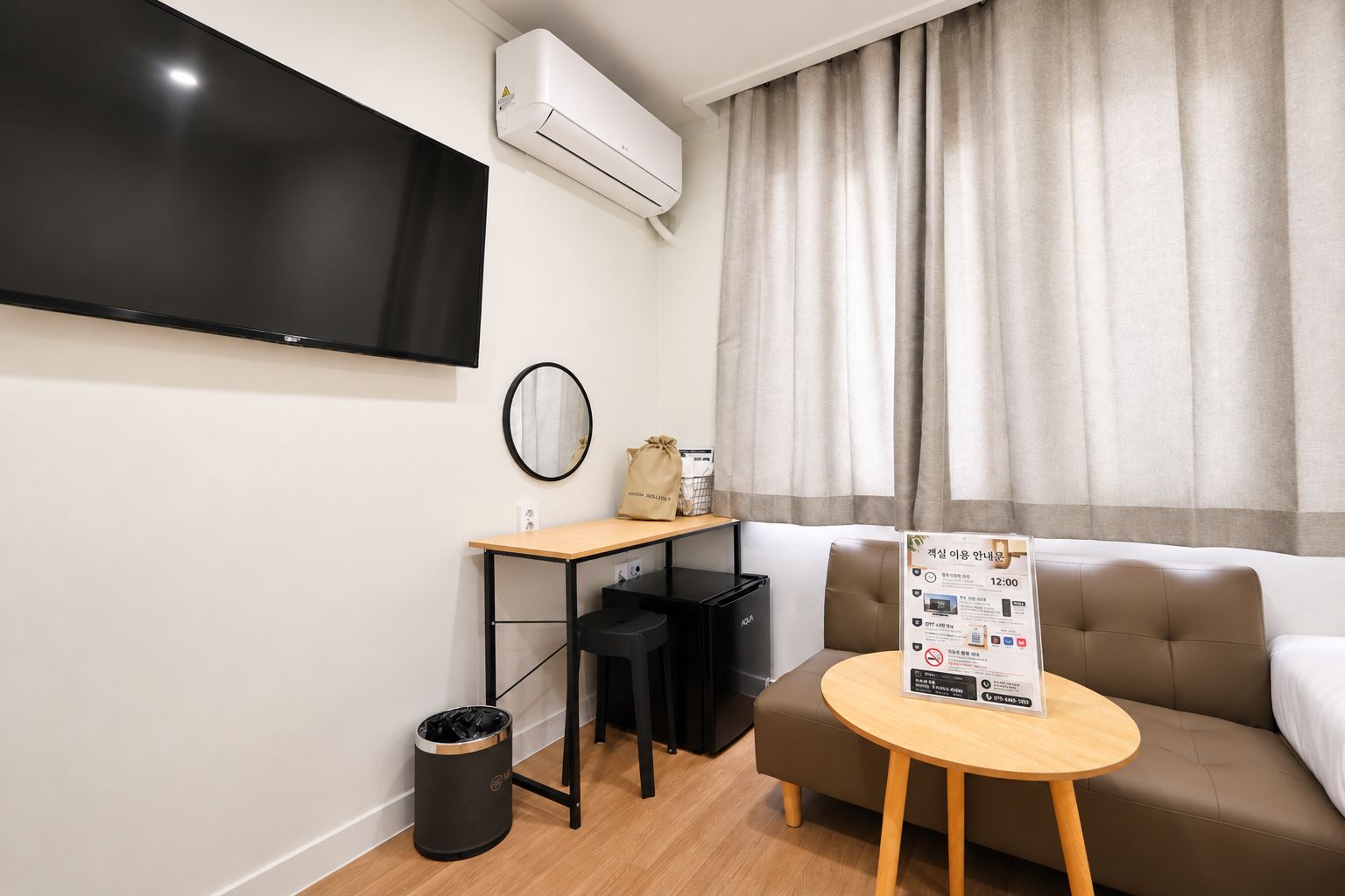 A modern hotel room with a flat-screen TV, a small desk with a chair, a sofa, and a round table.