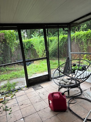 A room with a large glass door leading to a garden, a metal chair, and a red container on the floor.