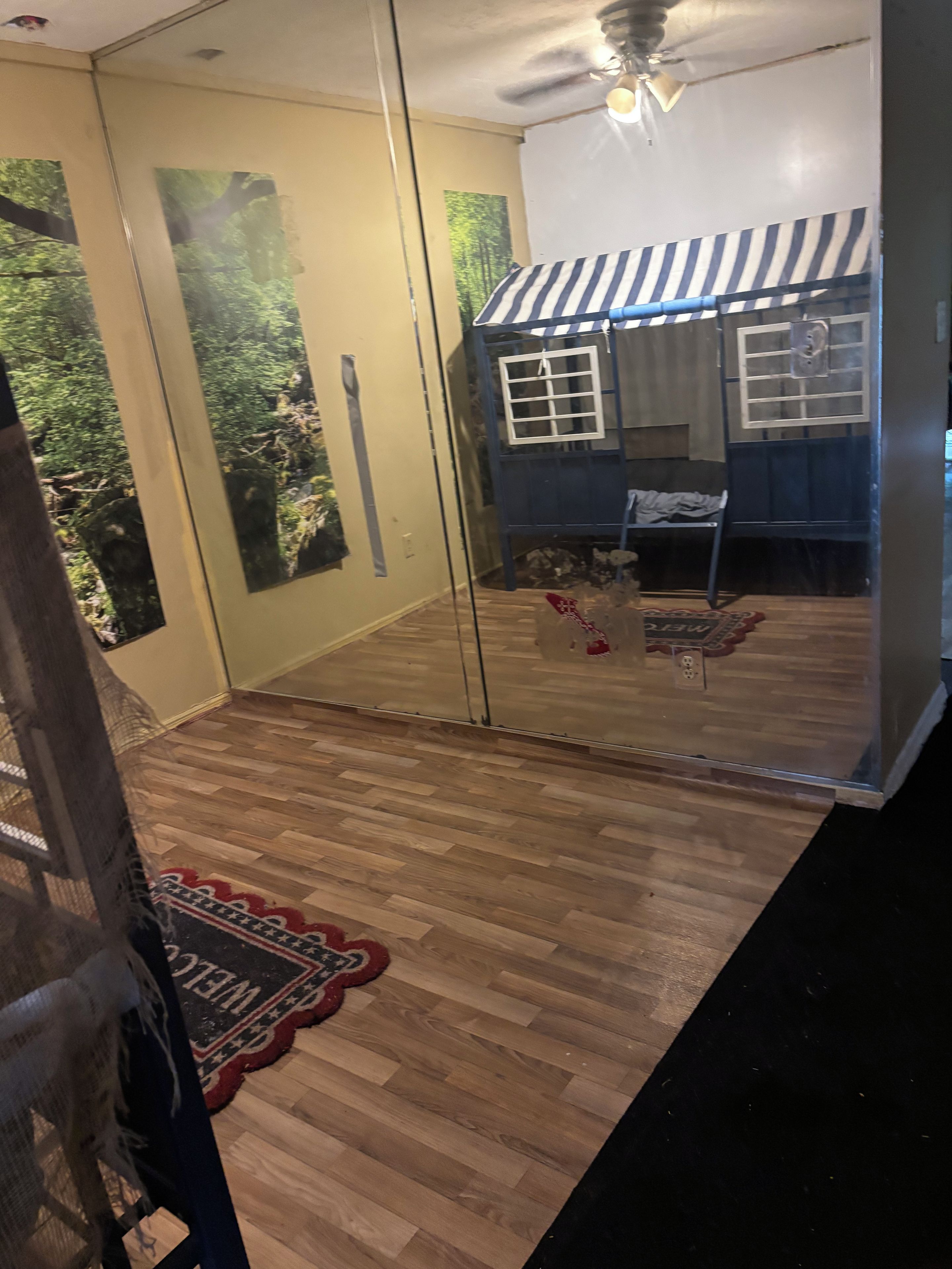 A room with a glass door leading outside, a wooden floor, a striped awning, and a small outdoor seating area.