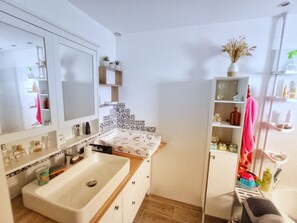 Une salle de bain avec un grand lavabo, un miroir et des étagères remplies de produits de toilette.