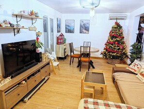 Un salon avec un téléviseur, une table à manger avec des chaises, un sapin de Noël et un canapé.
