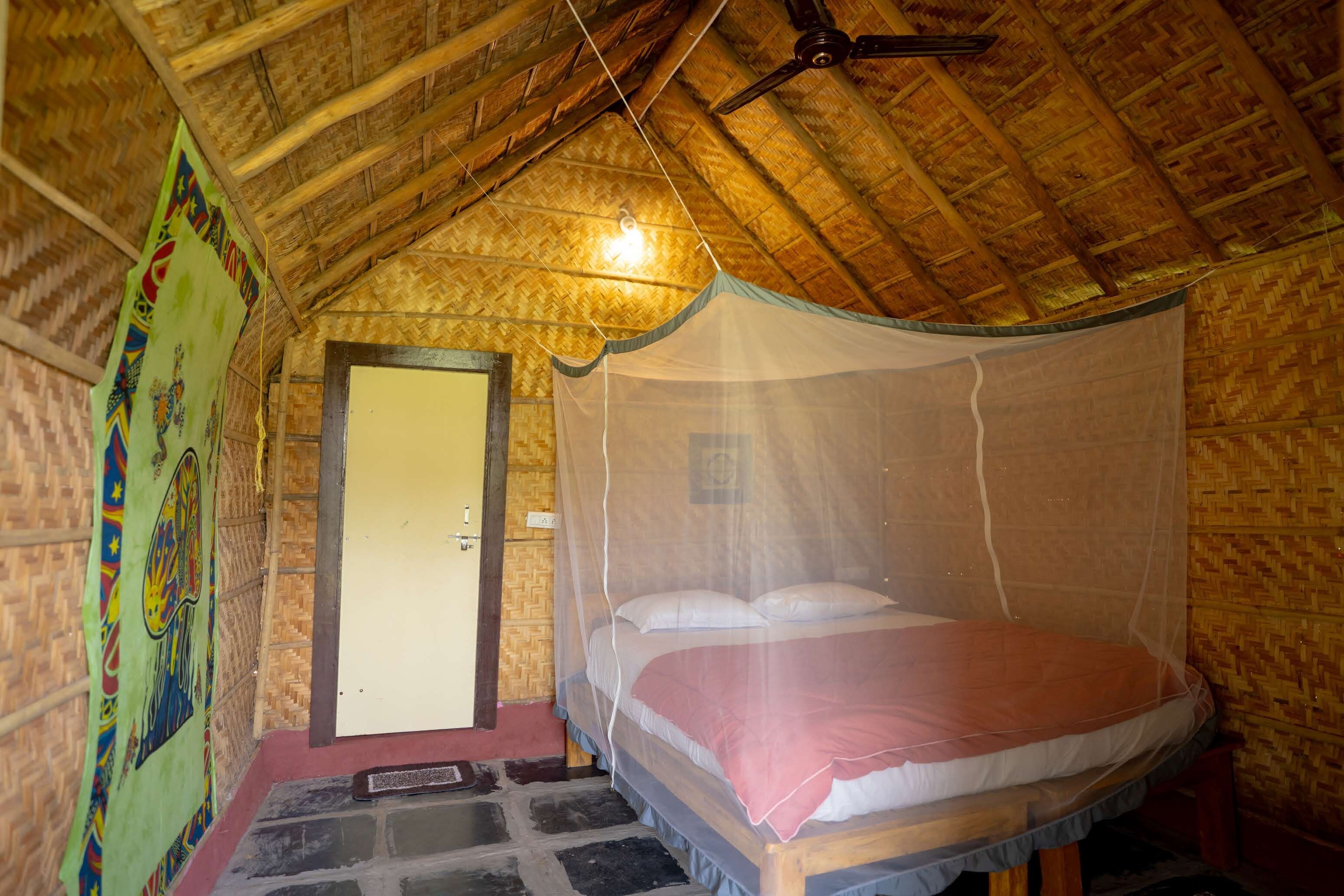 A room with a bed under a mosquito net, a wooden ceiling, and a door.