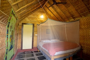 A room with a bed under a mosquito net, a wooden ceiling, and a door.