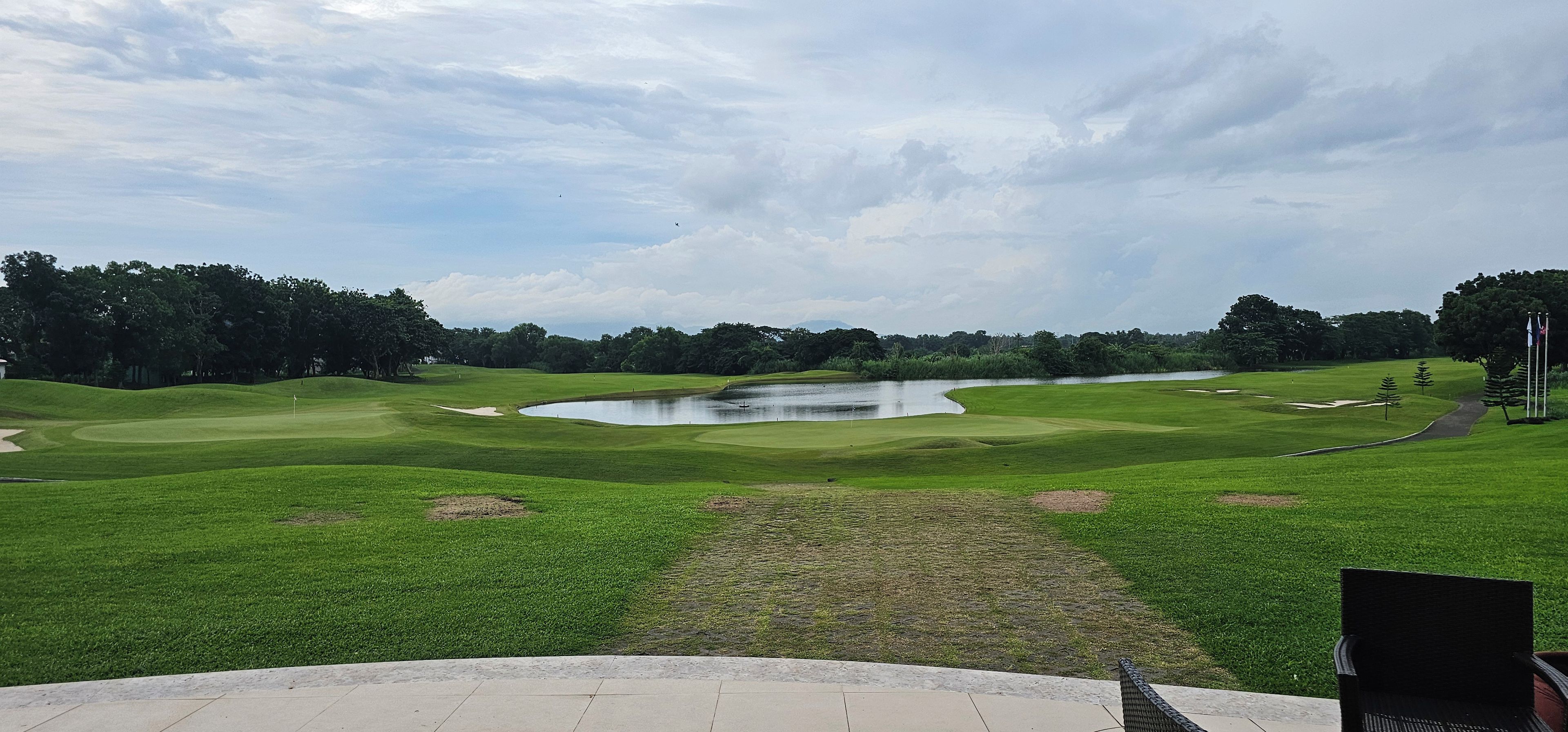 Um campo de golfe com lago, árvores e mastro.