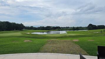 Um campo de golfe com lago, árvores e mastro.
