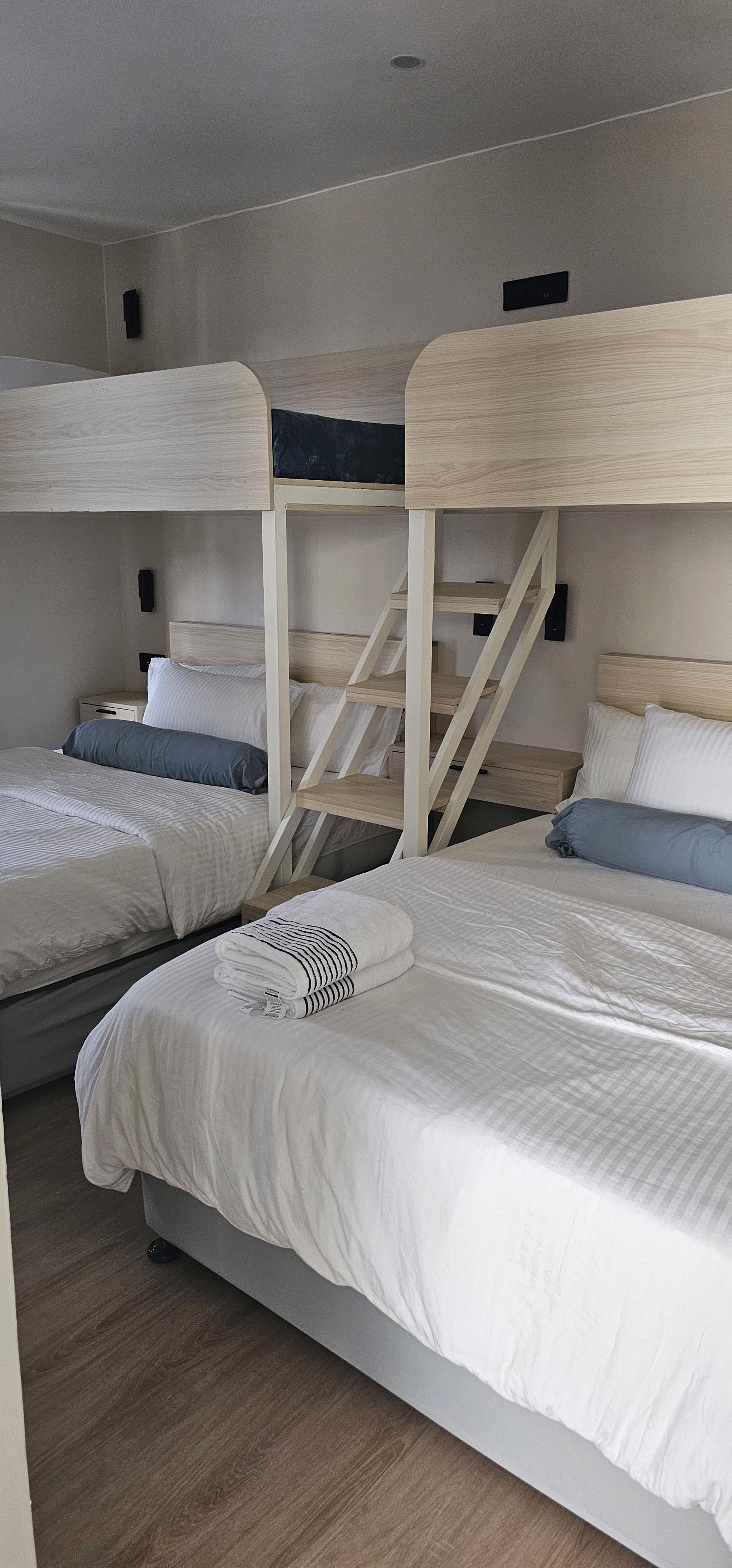 A room with bunk beds, a wooden staircase, and a bedside table with a lamp.
