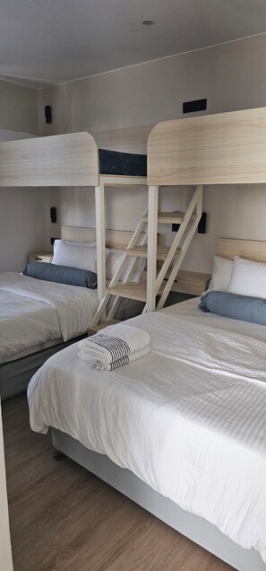 Una habitación con literas, una escalera de madera y una mesita de noche con lámpara.