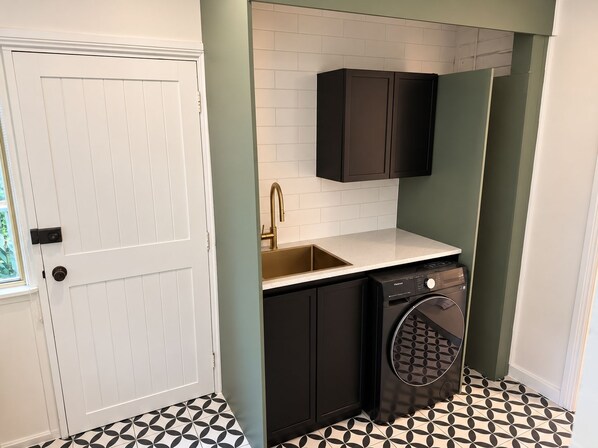 A compact kitchen with a white door, a sink with a gold faucet, black cabinets, and a washing machine.