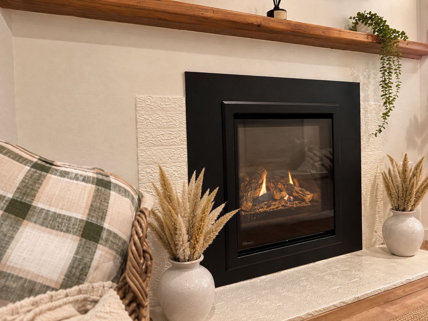 A fireplace with a modern design, flanked by two decorative vases with dried plants, set against a textured wall.