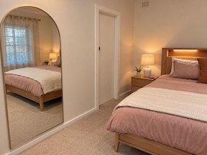 A bedroom with a mirrored wall, a wooden bed, a bedside table with a lamp, and a door.