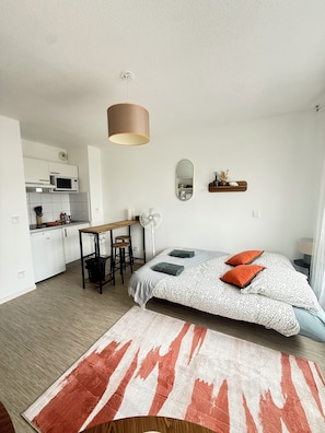 A compact hotel room with a kitchenette, a bed with patterned bedding, a small table, and a mirror.