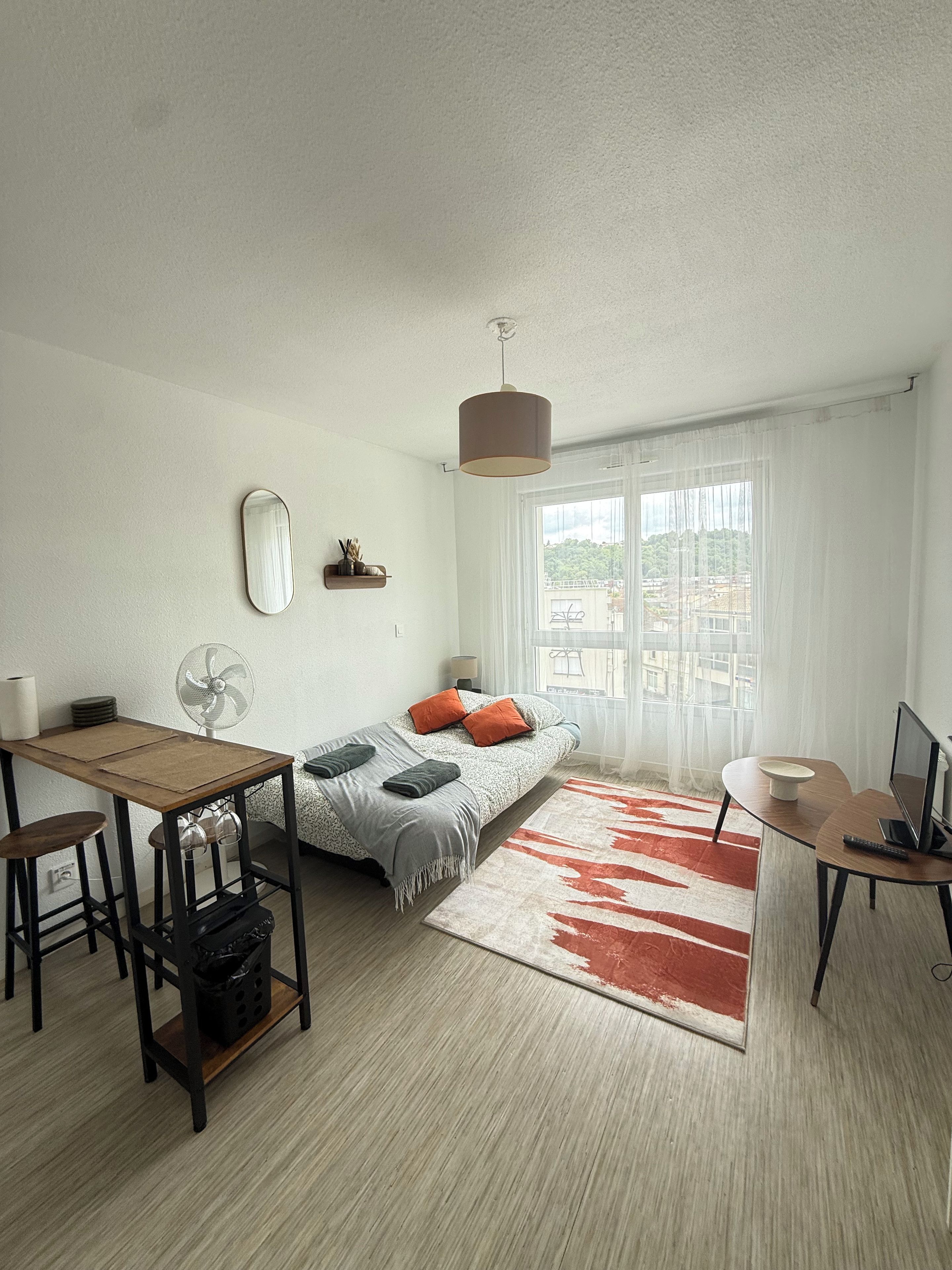 Une chambre moderne avec un lit, une table de chevet, une lampe et une vue sur la ville par la fenêtre.