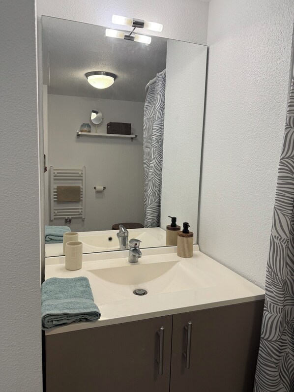 A bathroom with a white sink, a mirror, a towel, a shower curtain, and a shelf with toiletries.