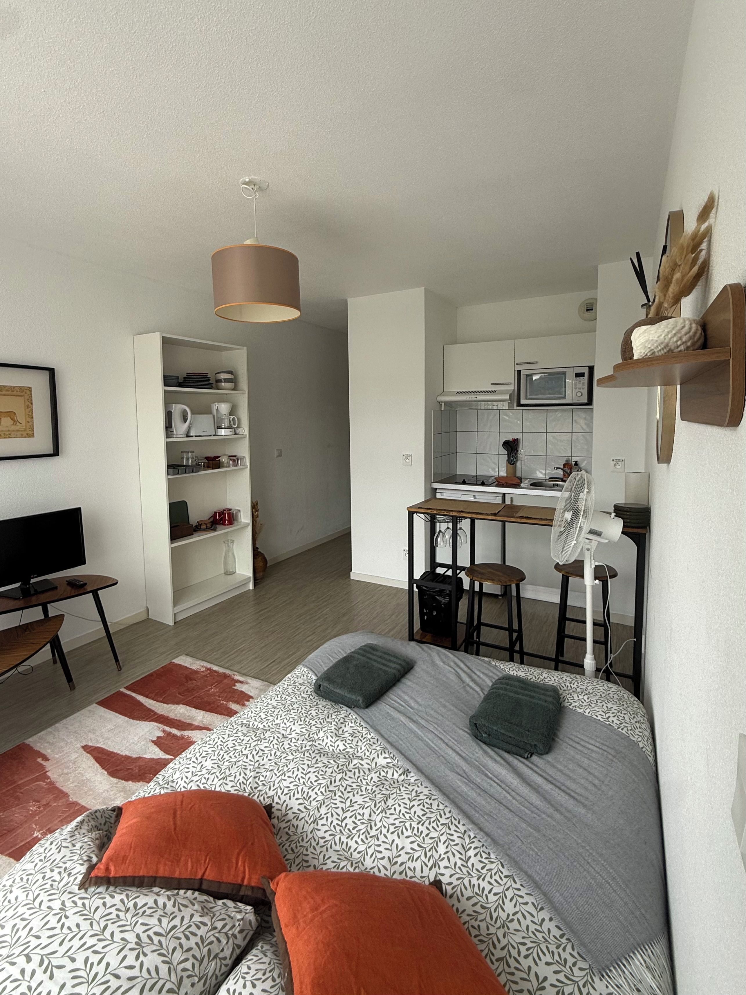 Ein gemütlicher, kompakter Wohnraum mit Bett, Fernseher, Küchenzeile und Essbereich.