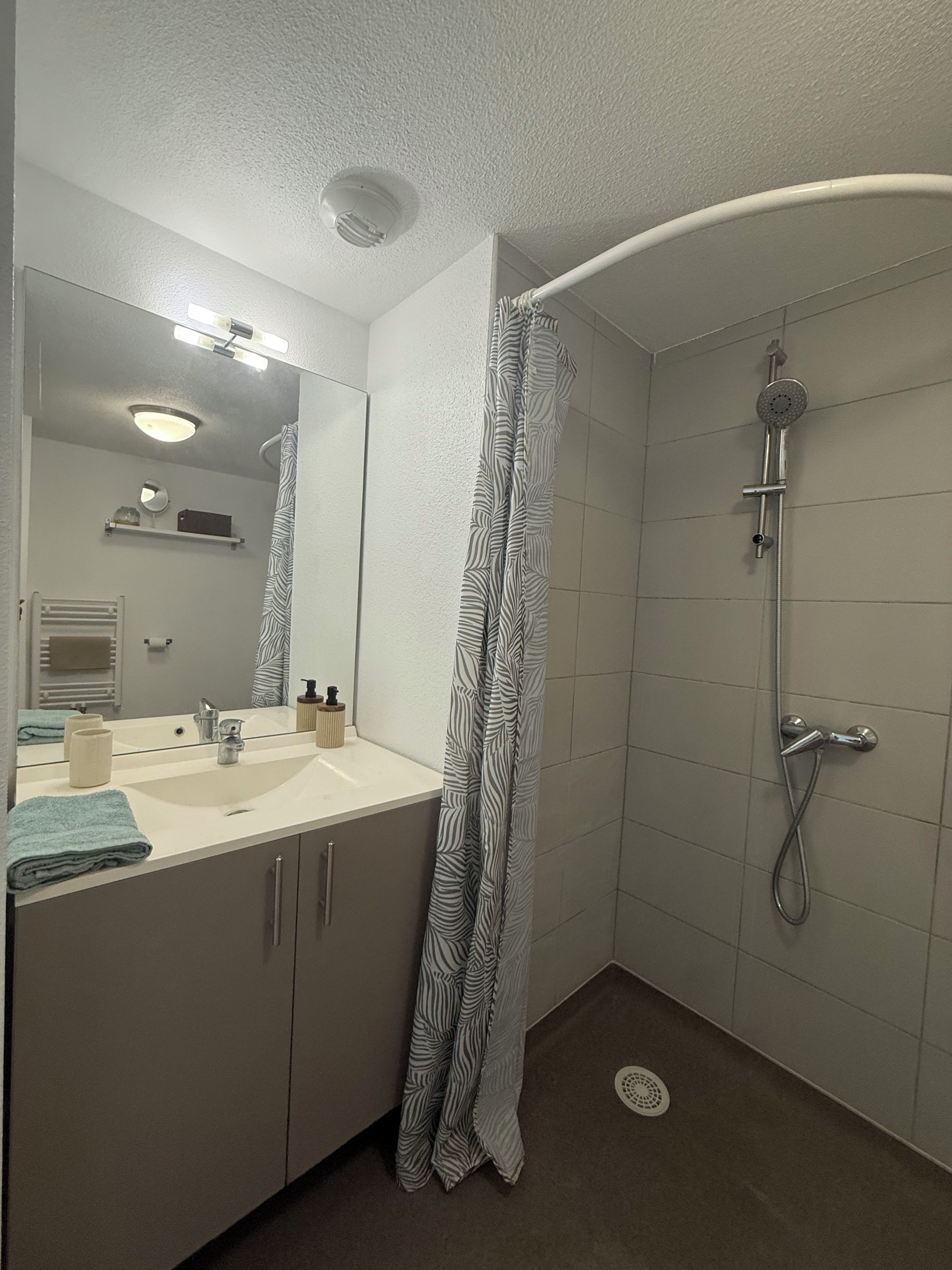 A bathroom with a shower, a sink, a mirror, and a towel rack.
