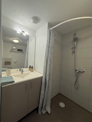 A bathroom with a shower, a sink, a mirror, and a towel rack.