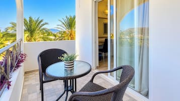 Un balcon avec une table en verre et deux fauteuils en osier, un pot de fleurs et une vue sur des palmiers et des montagnes.