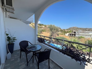 A balcony with a table and chairs, a potted plant, and a view of a building and landscape. - EO Rodou Lindou 407 (Faliraki)