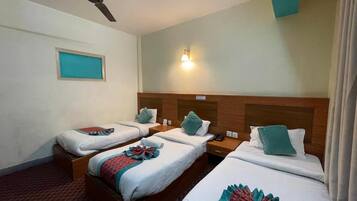 A hotel room with three single beds, a ceiling fan, a nightstand, and a wall-mounted light fixture.