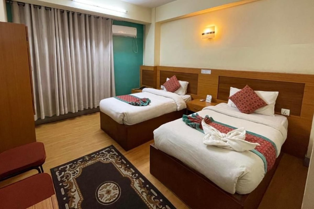 A hotel room with two beds, a wooden headboard, a desk, a chair, and a curtain.