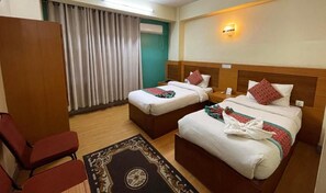A hotel room with two beds, a wooden headboard, a desk, a chair, and a curtain. - Hotel The President (Kathmandu)