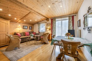 A cozy interior with a wooden ceiling, a dining area with a table and chairs, a sofa with cushions, and a wicker chair. - Country House 'Appartment Mit Schlafzimmer' with Mountain View and Wi-Fi (Kitzbühel)