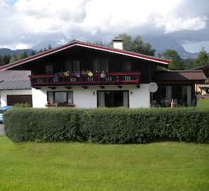 Ein zweistöckiges Gebäude mit Balkon, Garage und einer gepflegten Hecke davor.