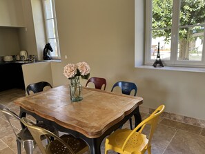 A dining area with a wooden table, chairs, a vase with flowers, a window with a view of trees, and a small Eiffel Tower model. - "La Vie est Belle" Gite - 6 pers, AC, in Domaine Pontourny with Indoor Pool (Beaumont-en-Véron)