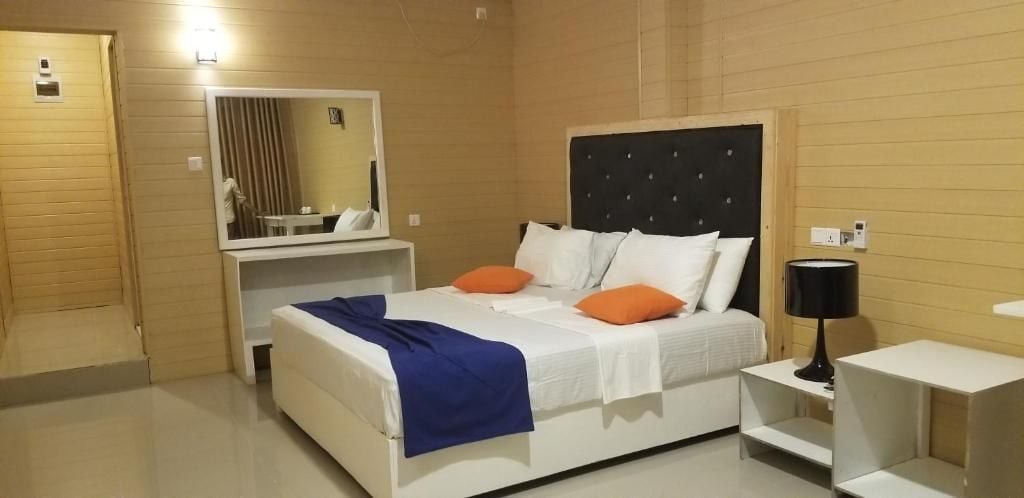 A hotel room with a bed, a bedside table, a lamp, and a mirror.