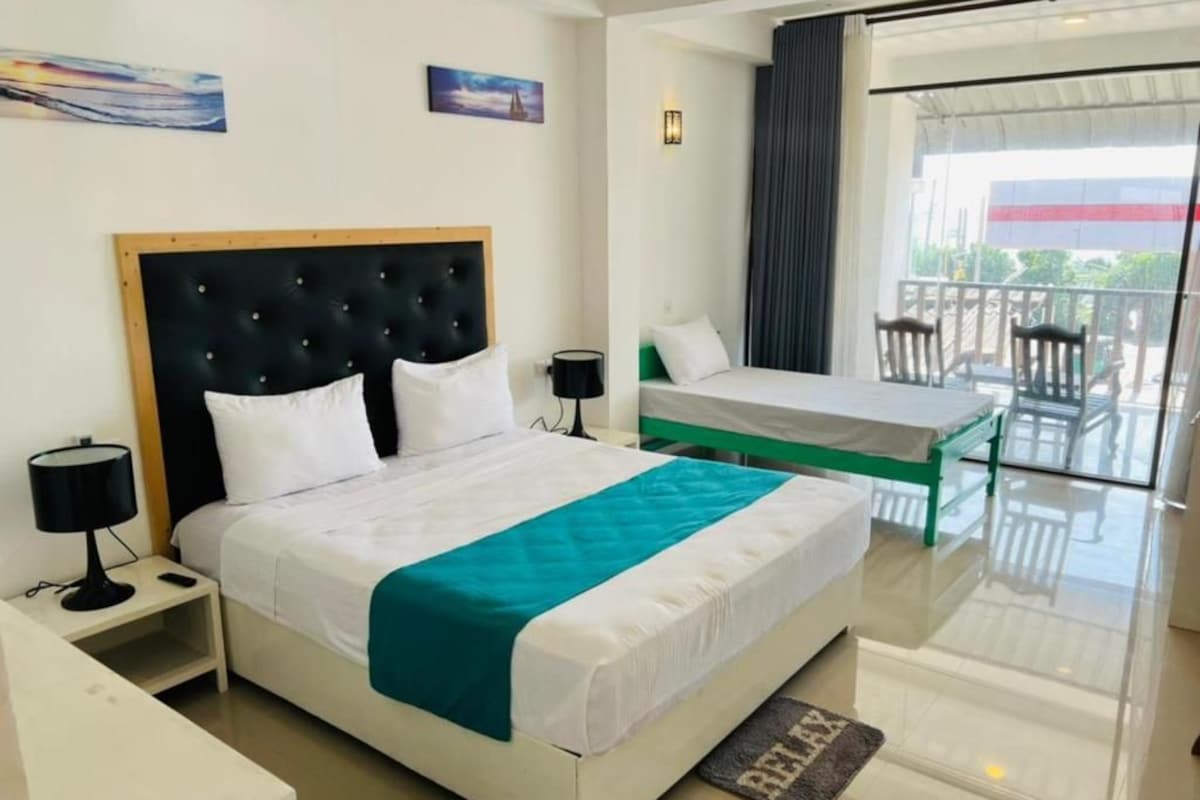 Habitación de hotel con una cama grande, una cama más pequeña, un balcón con sillas y vistas al exterior.